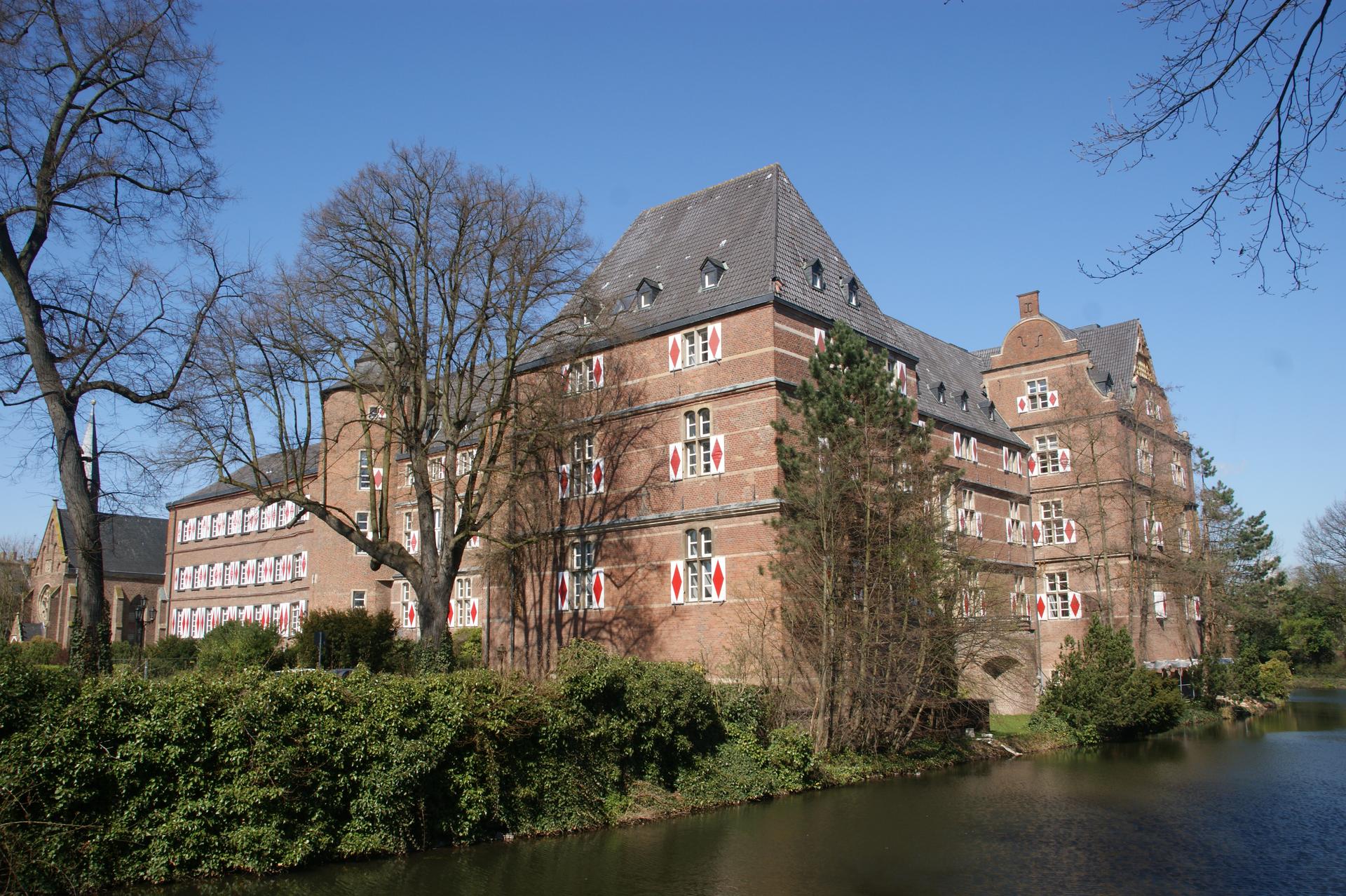 Schloss Bedburg, das backsteinerne Wasserschloss mit Schieferdach und Wassergraben unter blauem Himmel