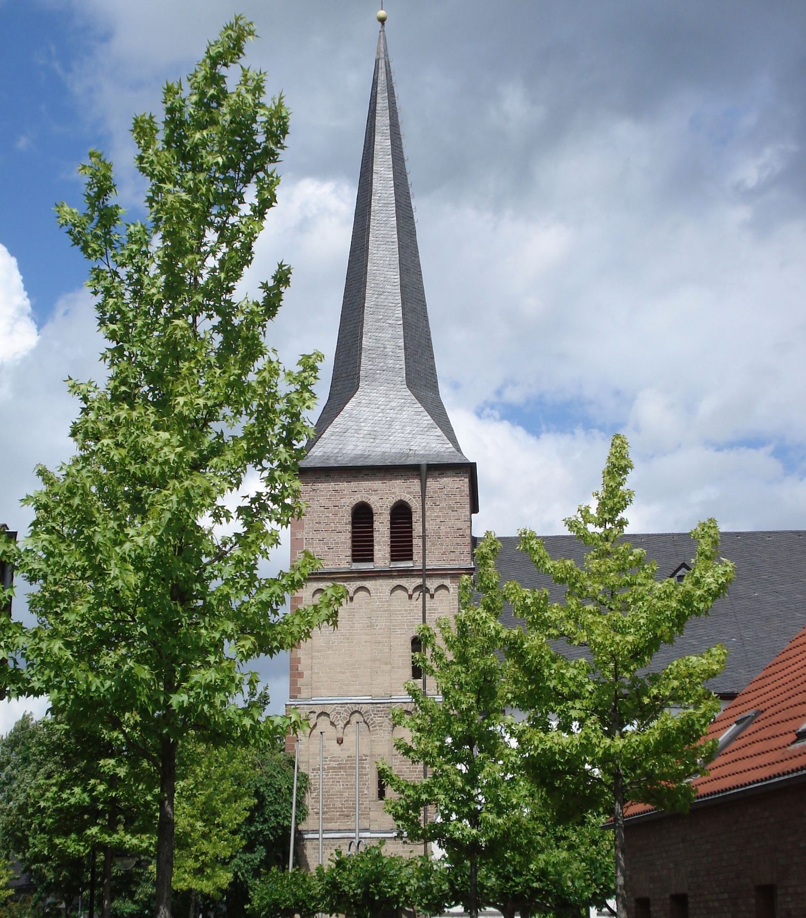 Katholische Pfarrkirche St. Mariä Geburt in Elsdorf, neugotische Backsteinkirche mit schiefergedecktem Turm über den Bäumen des Ortskerns